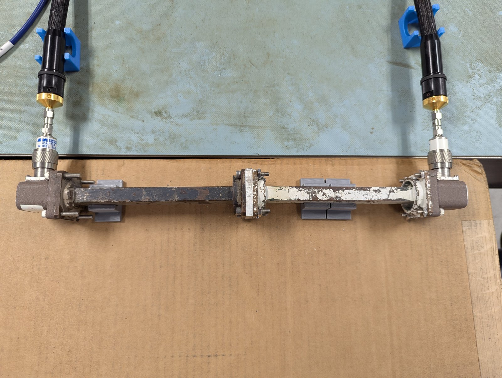 Waveguide measurement setup: two coax-to-waveguide adapters on the VNA cables, joined by two waveguide sections with the sample holder clamped between them